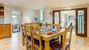 Zona pranzo con sedie di legno e un tavolo imbandito per quattro persone, cucina con mobili in legno, lavatrice e una finestra.