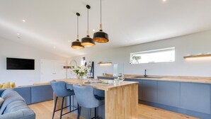 Una cocina moderna con una isla central, taburetes de bar, horno empotrado e iluminación colgante.