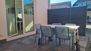 Eine Terrasse mit Tisch und Stühlen, eine Glastür zum Verschieben und ein dunkler Zaun.