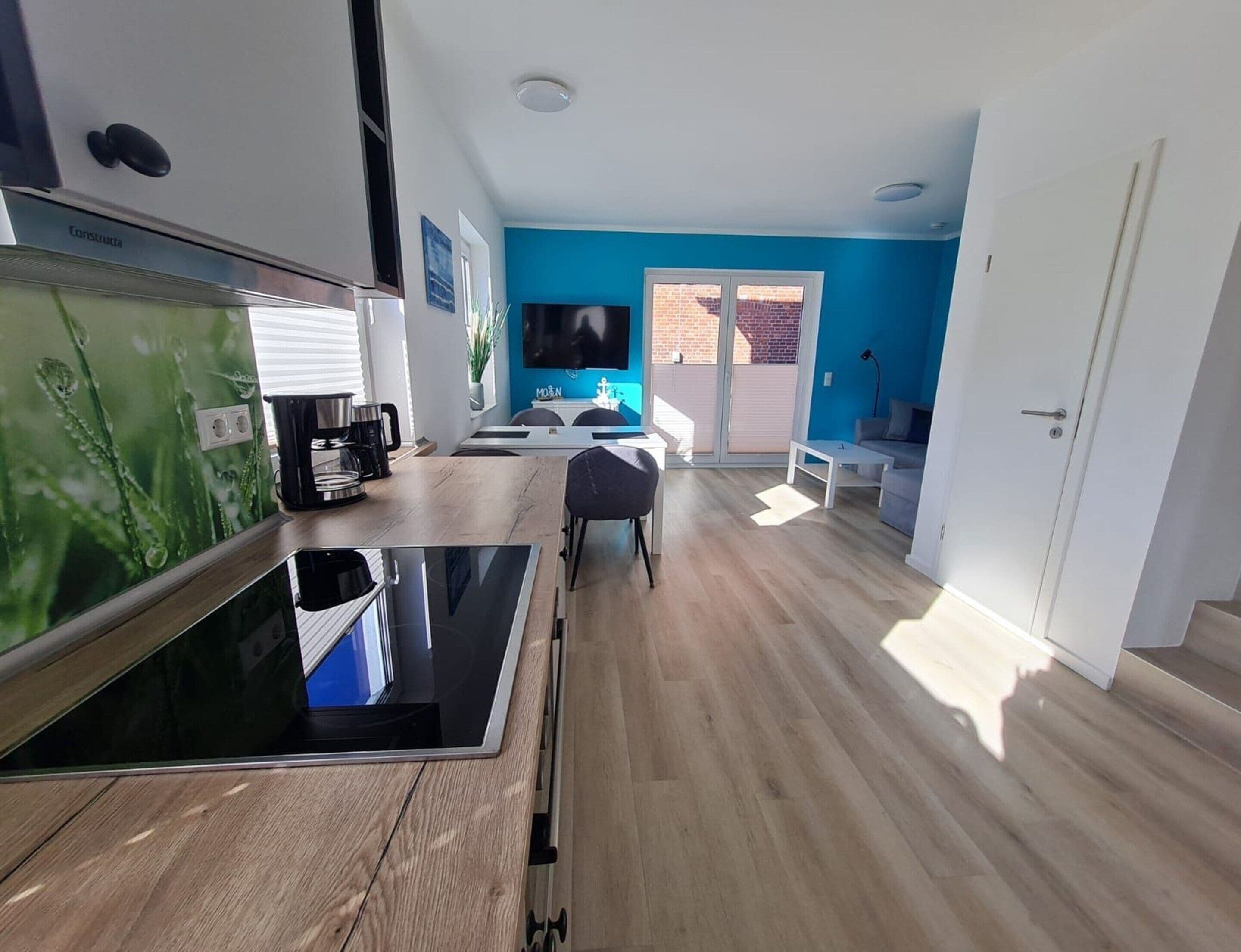 A modern kitchen with a built-in stove, a dining area with a table and chairs, and a living space with a sofa and a TV.