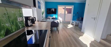 A modern kitchen with a built-in stove, a dining area with a table and chairs, and a living space with a sofa and a TV.