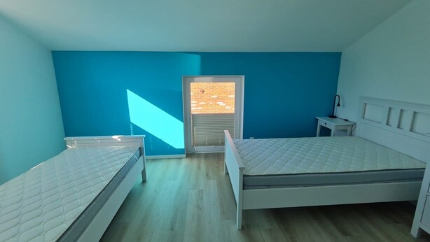 Ein Zimmer mit zwei Betten, einem Fenster mit Rollläden und einem kleinen Nachttisch.