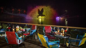 A nighttime outdoor seating area with colorful chairs and tables, overlooking a body of water with a fountain display. - Vidanta AAA 5 Star Diamond Resort - 1 BR Suite  w/ Daily 2 for 1 Golf Passes (Nuevo Nayarit)