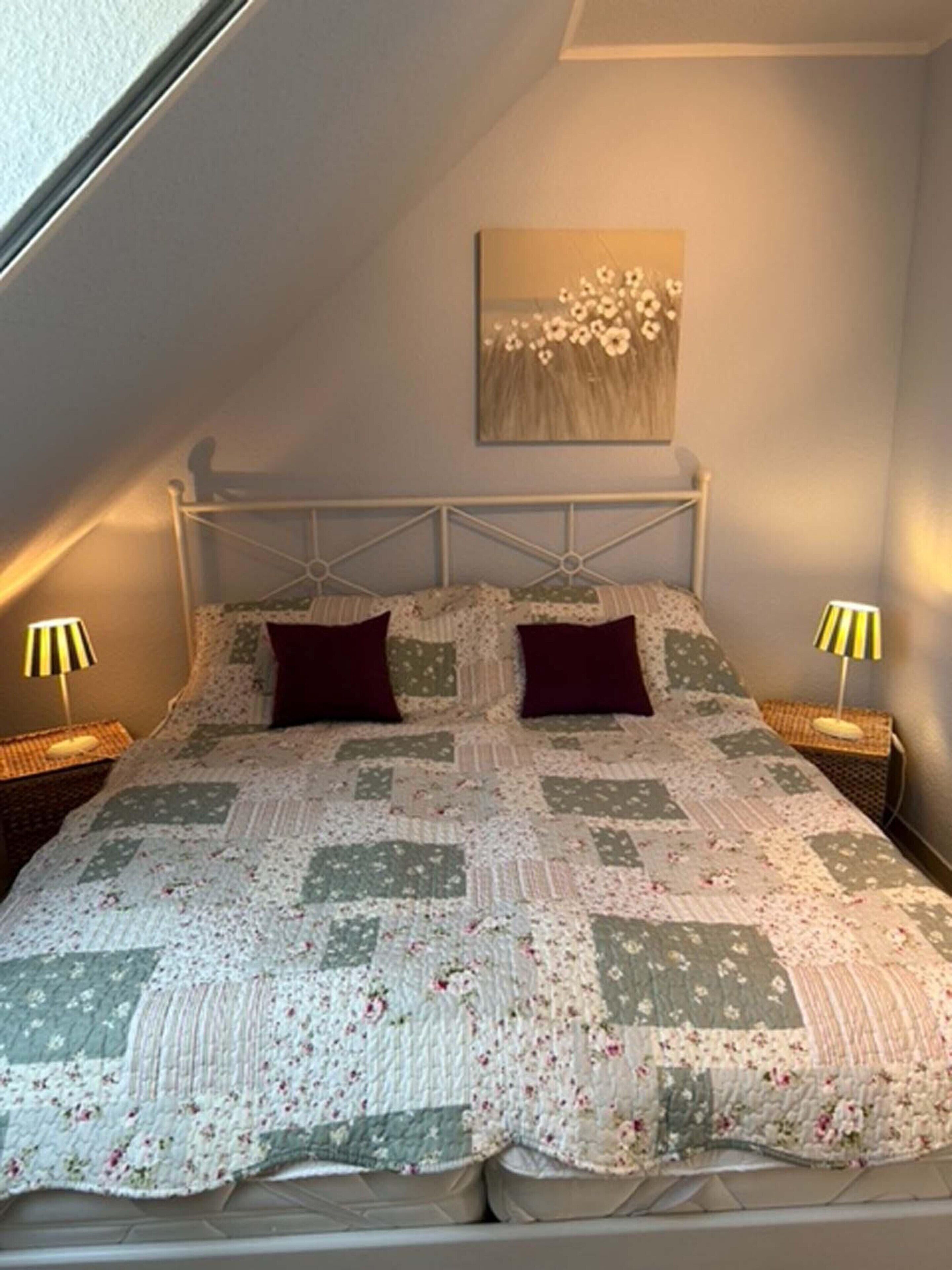 A bedroom with a bed, two bedside lamps, a wall-mounted painting, and a sloped ceiling.