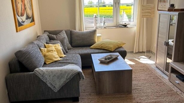Een woonkamer met een bank, een bijzettafeltje, een vloerkleed, een kast en een raam met uitzicht op een veld.