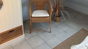 Een kamer met een schuine kap, een rieten stoel met kussen, een potplant en een kamerkleed met patroon.