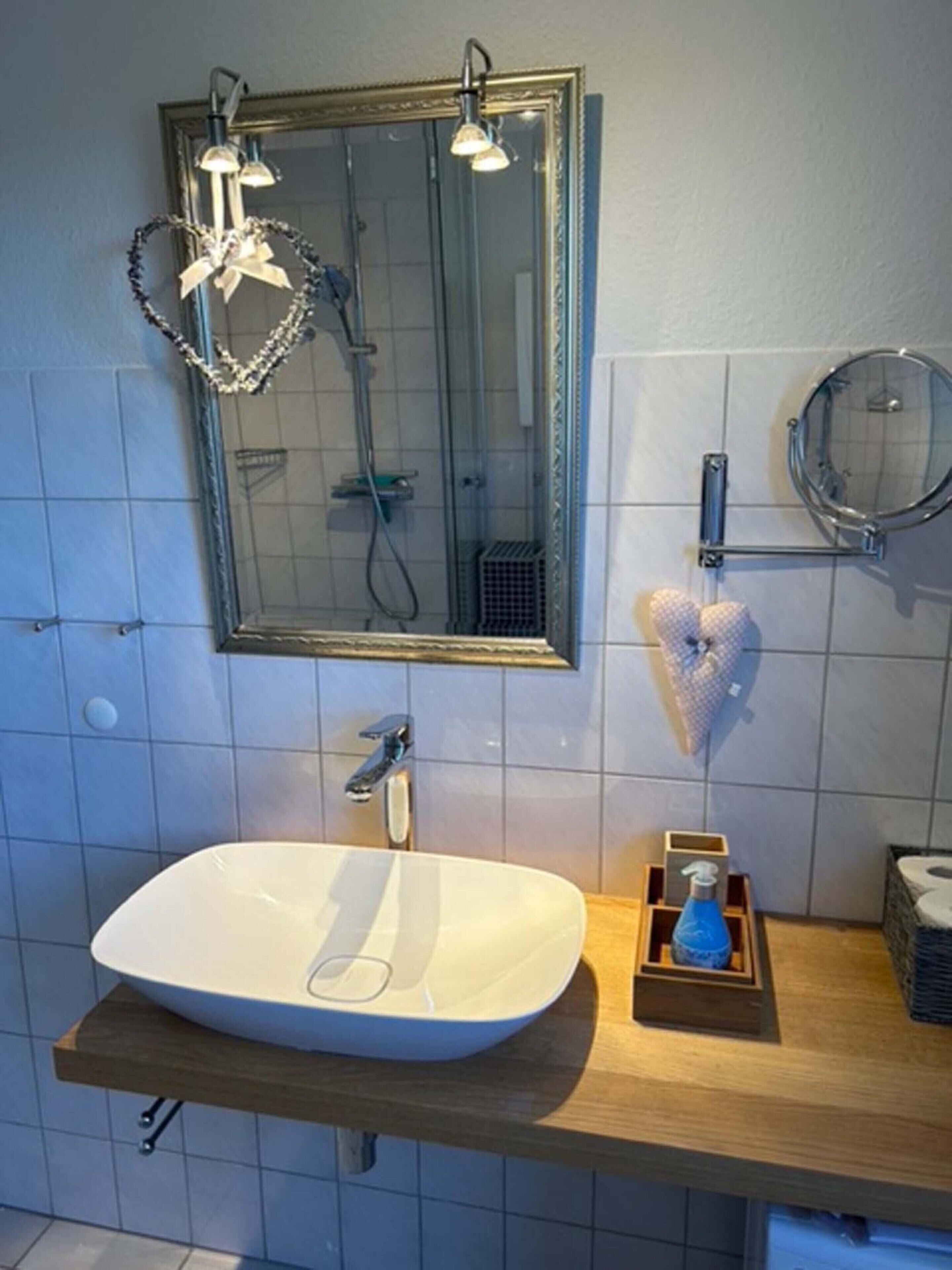 A bathroom with a large mirror, a white sink, a shower, and a towel rack.