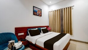 Una habitació d'hotel amb un llit, un butàc blau, una taula de nit amb una bandeja d'objectes i un quadre a la paret.