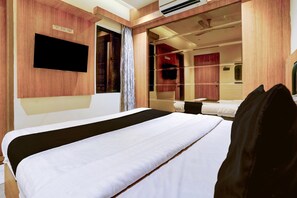 Ein Hotelzimmer mit einem großen Bett, einem flachbildfernseher an der Wand, einem Spiegel und einem Fenster mit Vorhängen.