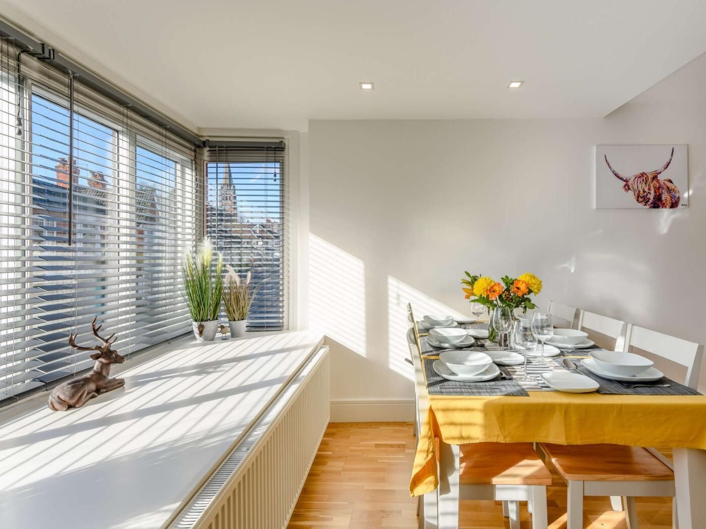 A dining area with a table set for four, a radiator, and a window with blinds.