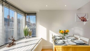 Un coin repas avec une table dressée pour quatre personnes, un radiateur et une fenêtre avec des stores.