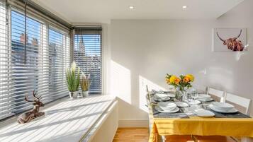 A dining area with a table set for four, a radiator, and a window with blinds.