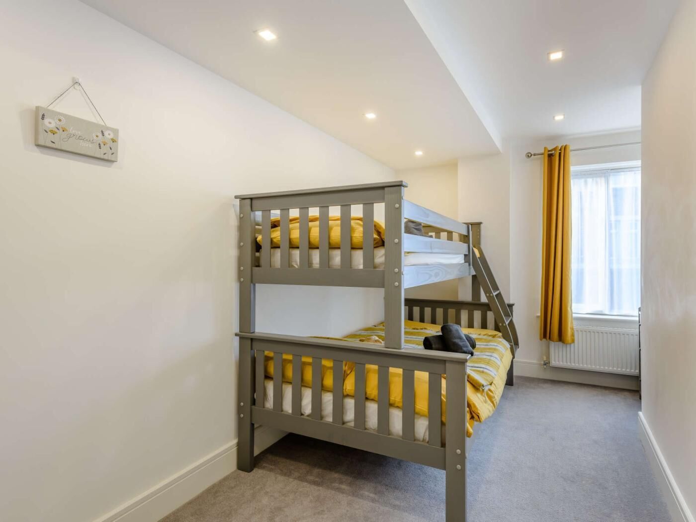 A bunk bed room with a ladder, a window with curtains, and a wall-mounted decoration.