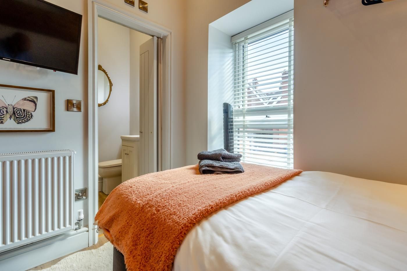 A bedroom with a bed, a radiator, a window with blinds, and a door.
