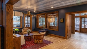 A room with a wooden ceiling, large windows, a red patterned rug, and a wooden table with chairs. - Tumbling River Ranch (Grant)