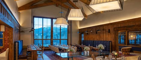 Un comedor espacioso con techos altos, vigas de madera y amplios ventanales que ofrecen vistas al exterior.