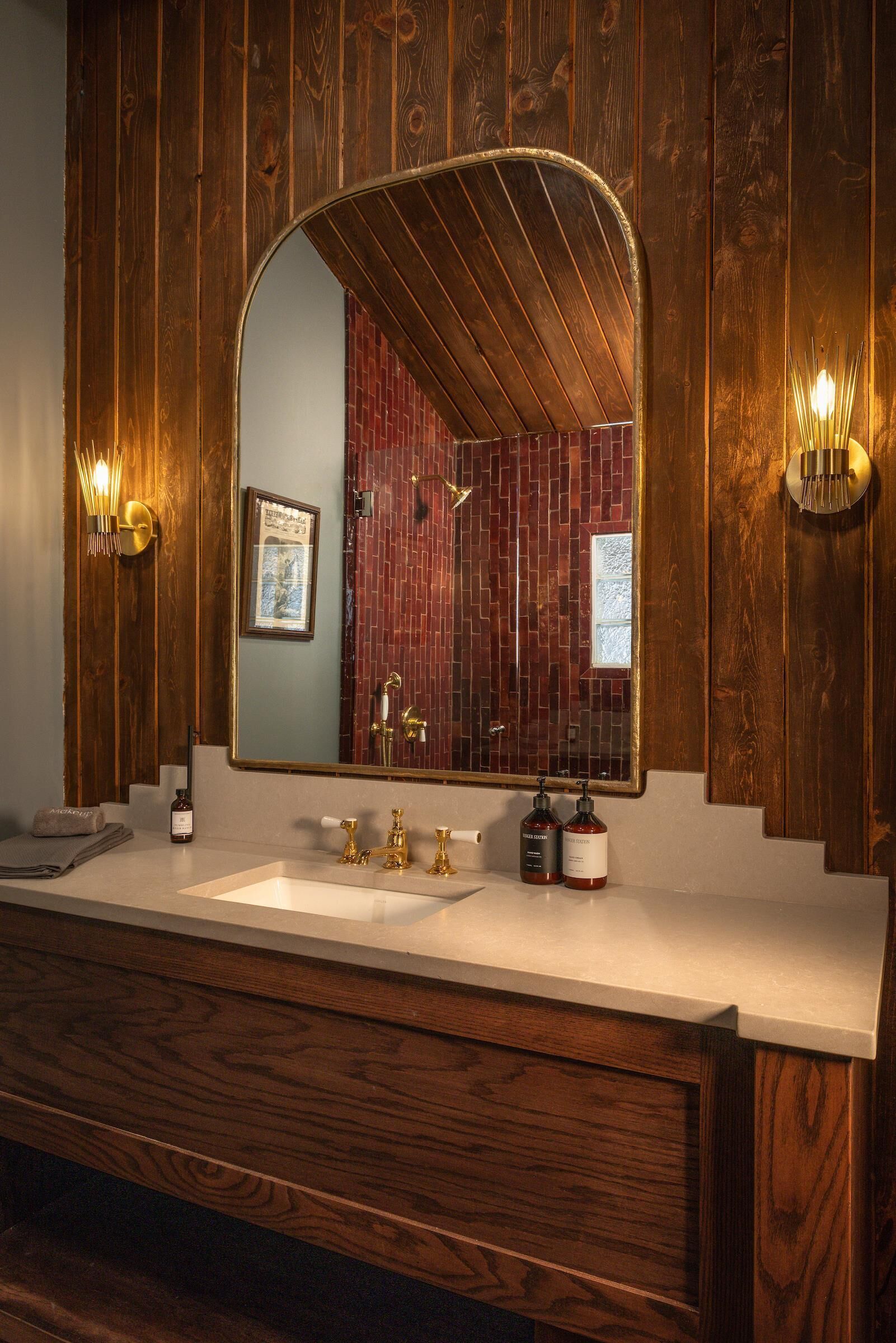 A bathroom with a wooden vanity, a large mirror, and two wall-mounted light fixtures.