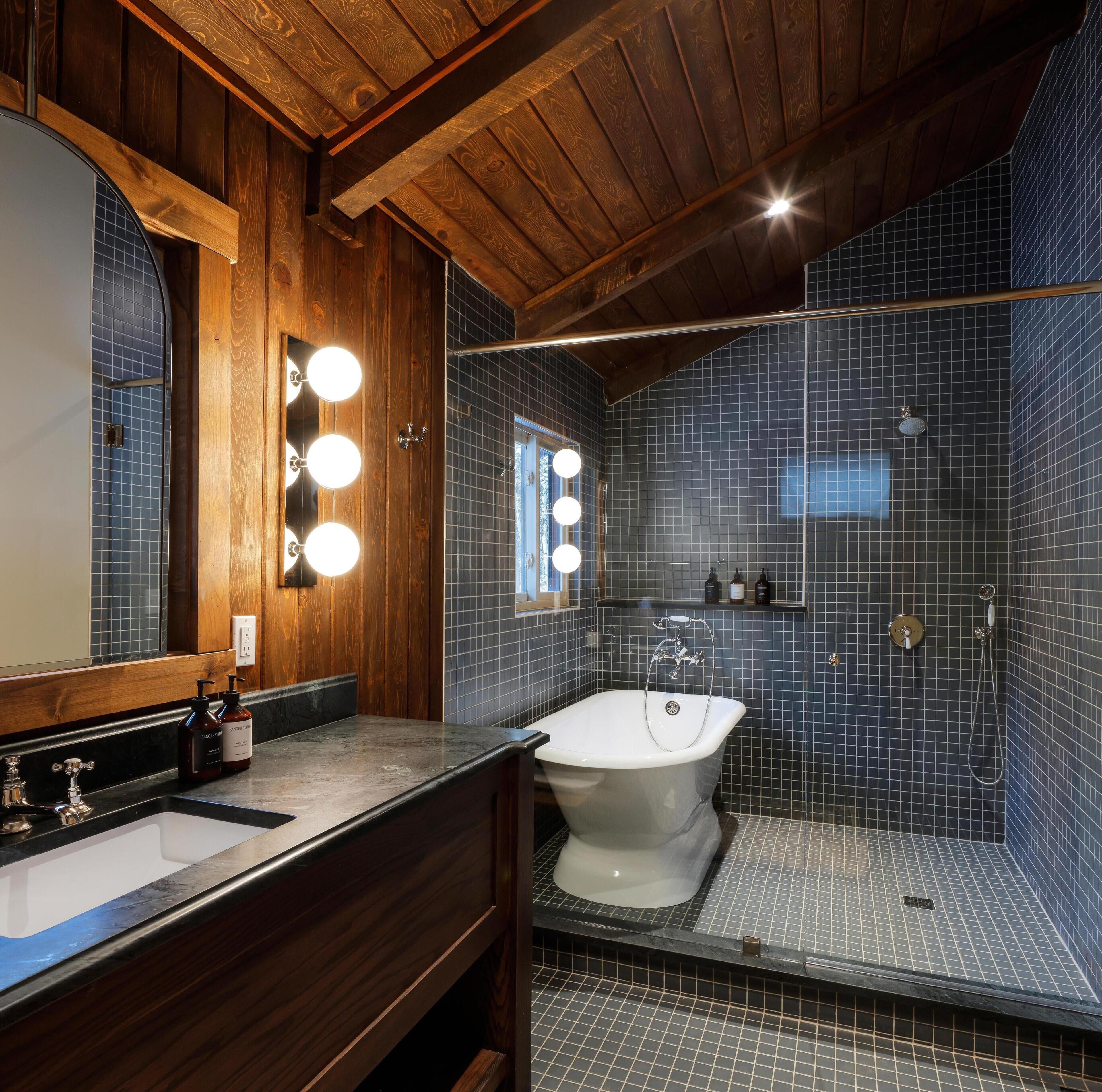 A bathroom with a wooden vanity, a freestanding bathtub, and a shower area with blue-tiled walls.