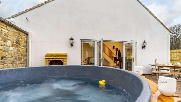 Ein Whirlpool mit einer Ente, einer Holzbank und einem Tisch mit einer Tasse.