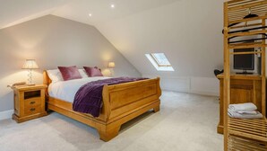 Ein Schlafzimmer mit schrägem Dach, einem Bett, Nachttischlampen, einem Holzschrank und einem Dachfenster.