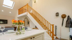 Eine Küche mit weißer Arbeitsplatte, einer Holztreppe und einem Essbereich mit Sofa und Tisch.