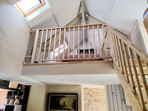 Une pièce aux hauts plafonds, dotée d’une lucarne, d’un escalier en bois et d’une œuvre d’art encadrée accrochée au mur.
