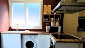 Eine kleine Küche mit Waschmaschine, Mikrowelle und einem Fenster über der Spüle.