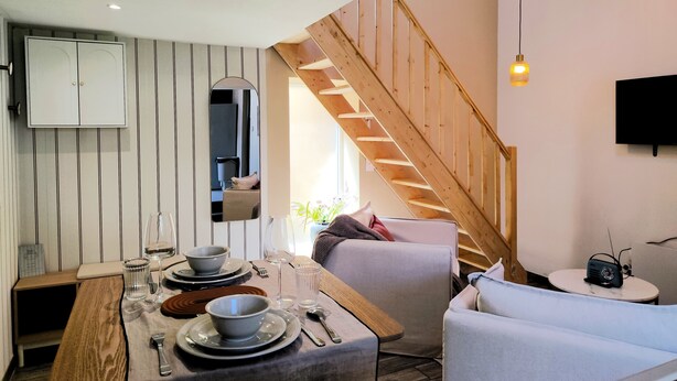 Eine moderne Küche mit Esstisch für zwei Personen, einer Holztreppe und einem an der Wand befestigten Flachbildfernseher.