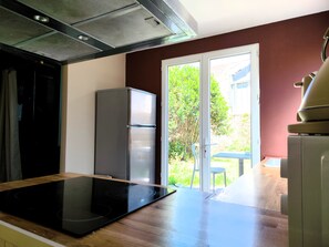 Une cuisine dotée d’une plaque de cuisson à induction noire, d’un réfrigérateur en acier inoxydable et d’une porte-fenêtre coulissante donnant sur un patio.