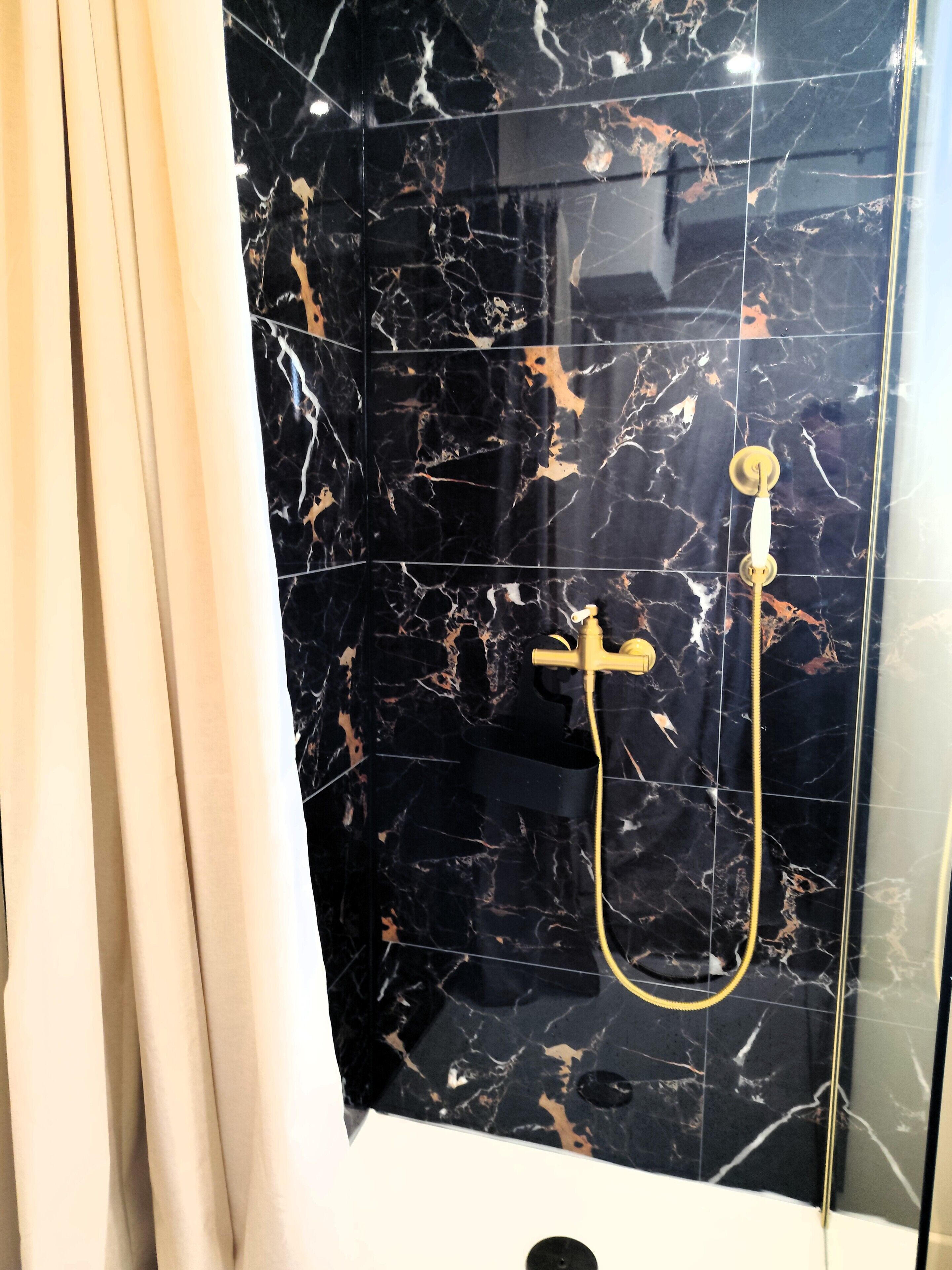 A bathroom with black marble tiles, a gold showerhead, and a curtain.