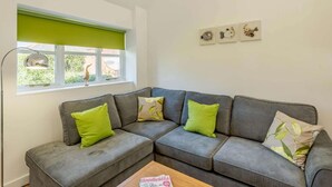 A grey sectional sofa with green cushions, a wooden coffee table, a floor lamp, and a window with a green blind. - 2 Bed in Louth (oc-86797) (Fotherby)