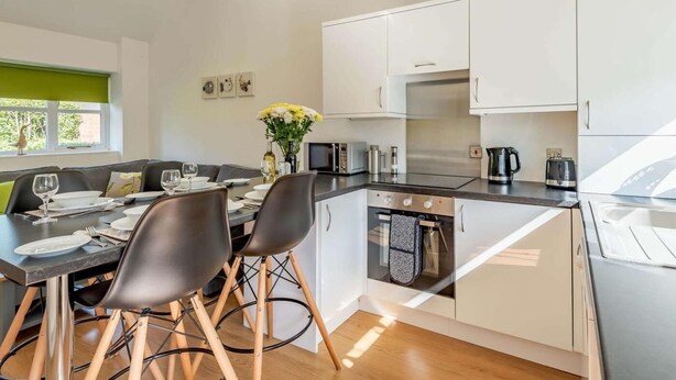 A modern kitchen with white cabinets, a central island, and a dining area with a table and chairs. - 2 Bed in Louth (oc-86797) (Fotherby)