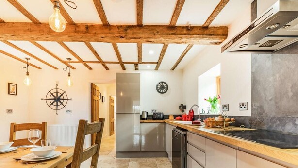 Een keuken met een houten plafond, een roestvrijstalen koelkast, een spoelbak en een eethoek met een tafel en stoelen.