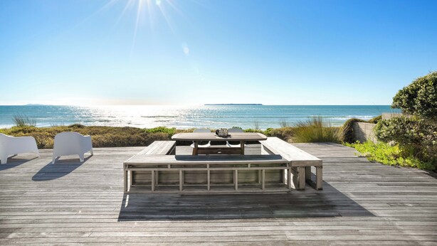Una terraza de madera con una mesa de picnic y sillas blancas con vista al océano.