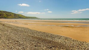 Ein Strand mit Kieselsteinen, ein Sandufer und eine hügelige Landschaft im Hintergrund.