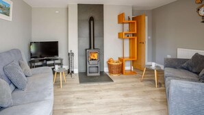 Ein modernes Wohnzimmer mit Kamin, grauen Sofas, einem Fernseher und einem Bücherregal aus Holz.