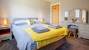 Ein Schlafzimmer mit einem Bett, Nachttischen, einer Kommode, einem Spiegel und einer Tür.