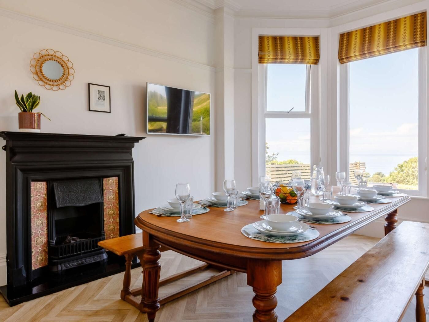 Comedor con chimenea, una larga mesa dispuesta para seis personas y vistas a través de grandes ventanales.