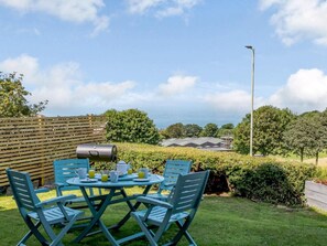 A patio with a round table and chairs, a barbecue grill, and a view of the sea. - 6 Bed in Ilfracombe (oc-86780) (Ilfracombe)