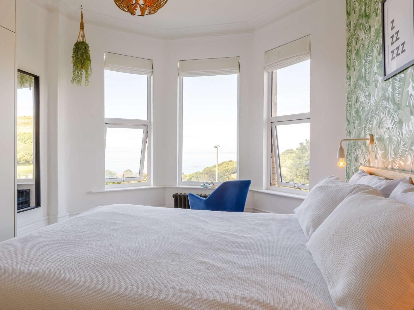 A bedroom with a large bed, three windows, and a hanging plant.