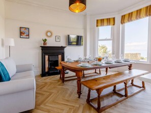 Ein Essbereich mit Holztisch, gedeckt für vier Personen, einem Kamin, einem Fernseher und Blick ins Freie.
