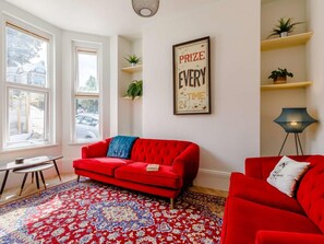 Ein Wohnzimmer mit einem roten Sofa, einem gemusterten Teppich, einem gerahmten Motivationsposter und Blick ins Freie durch große Fenster.