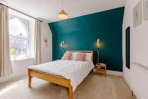 A bedroom with a bed, bedside tables, and a window with curtains. - 6 Bed in Ilfracombe (oc-86780) (Ilfracombe)