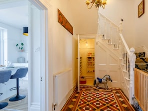 A hallway with a patterned floor, a staircase with white railings, and a dining area with chairs and a table. - 6 Bed in Ilfracombe (oc-86780) (Ilfracombe)