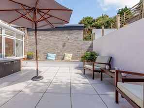 Eine Terrasse mit gefliestem Boden, einer hölzernen Bank, einem Tisch mit Tassen und einem großen Sonnenschirm.