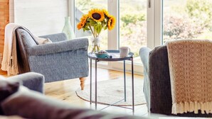 Ein Zimmer mit einer Couch, einem kleinen Tisch mit einer Sonnenblumenvase und Blick durch eine Glastür.