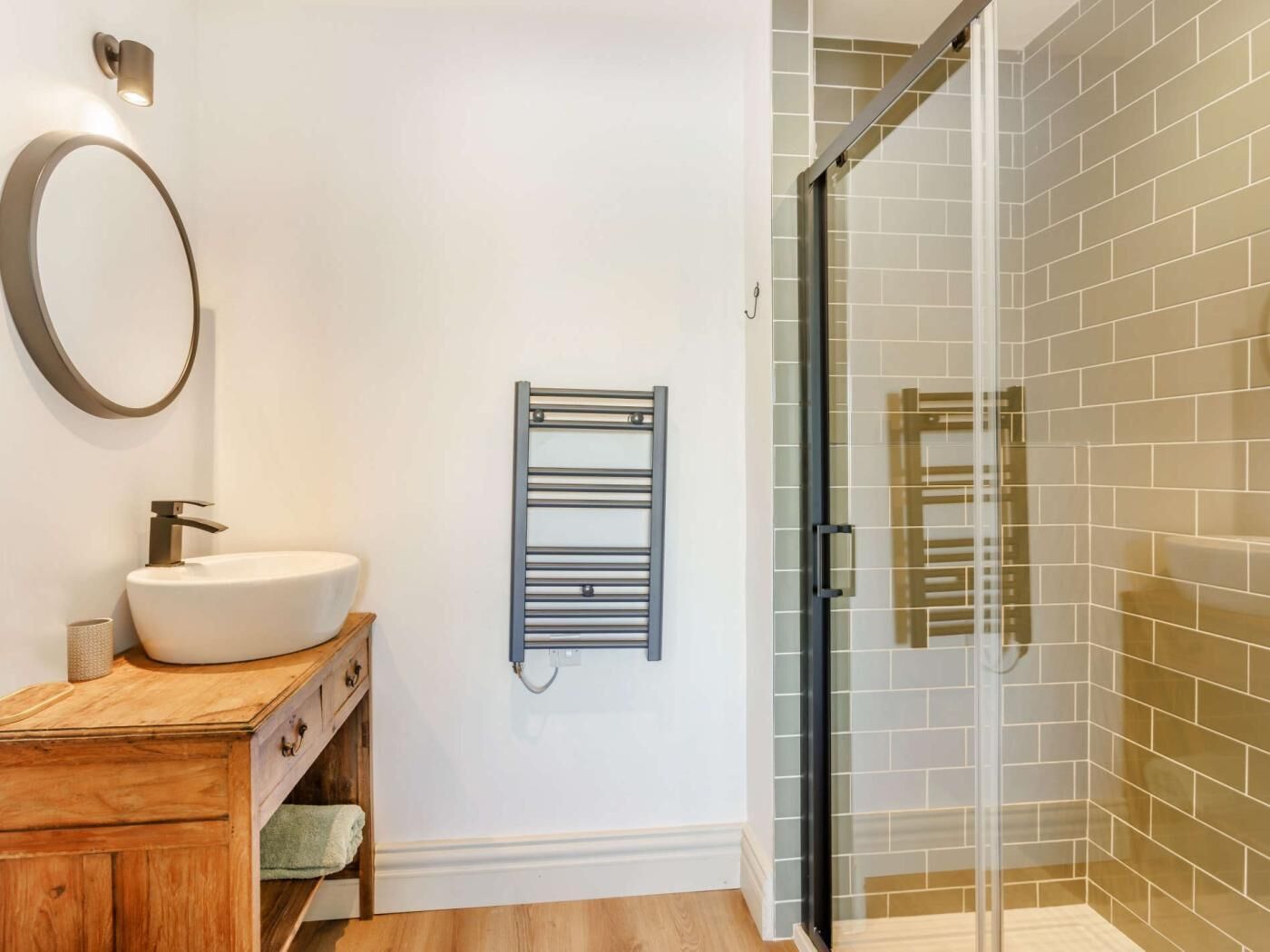 A bathroom with a white sink, wooden vanity, a towel rack, and a glass shower enclosure.