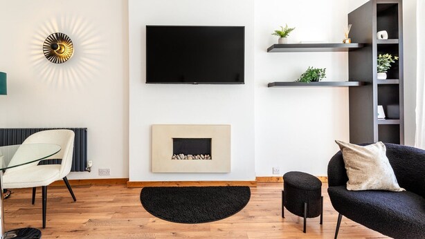 Een moderne woonkamer met een flatscreen televisie, een ingelijst kunstwerk, een open haard, een bank, een fauteuil en inbouwkasten met planten.