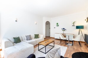 A modern living room with a sofa, coffee table, and a dining area with chairs and a table. - Knightsbridge Apartment by Harrods (London)
