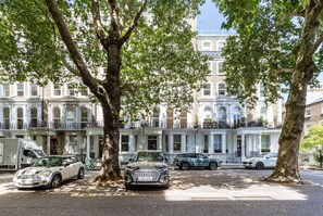 A row of classic townhouses with large windows, parked cars, and trees in the foreground. - Knightsbridge Apartment by Harrods (London)